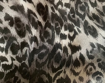 Puede incluir: Una bufanda blanca con estampado de leopardo negro y gris y un diseño de cadena roja.