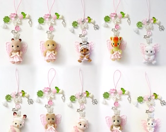 May include: A collection of hanging ornaments featuring small animal figures with pink fairy wings and dresses. Each ornament has a decorative top with pink, white, and green accents, including flowers, bows, and beads. The animals include bears, bunnies, and a giraffe.