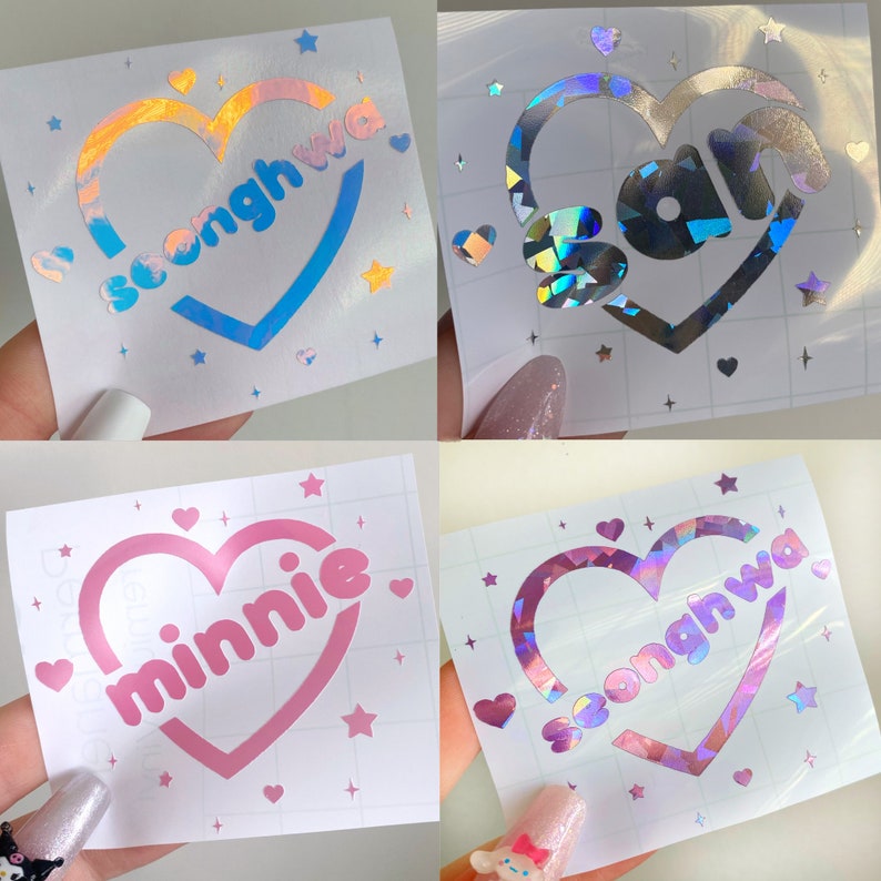 May include: Four different holographic vinyl stickers with heart-shaped designs. Each sticker features a different name: "Seonghwa", "San", "Minnie", and "Seonghwa". The stickers are on a white background with small stars and hearts.