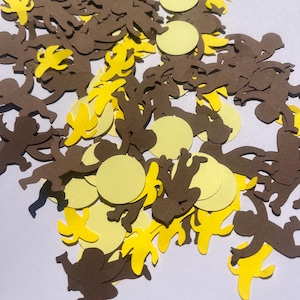 May include: A collection of brown monkey and yellow banana cutouts, along with yellow circle cutouts, scattered across a white surface. The cutouts are made of paper and are likely intended for crafting or decoration.