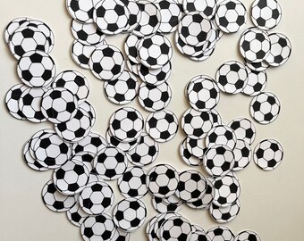 May include: A large group of black and white soccer ball confetti. The confetti is scattered on a white surface.