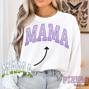 May include: White long-sleeved sweatshirt with the word "MAMA" in purple and a purple arrow pointing upwards. The word "MAMA" is also written in green and blue below the arrow.