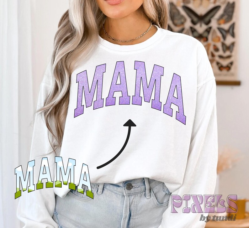 May include: White long-sleeved sweatshirt with the word "MAMA" in purple and a purple arrow pointing upwards. The word "MAMA" is also written in green and blue below the arrow.