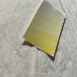 May include: A small, rectangular, silver-colored sticker with a yellow gradient and a small hole in the center.
