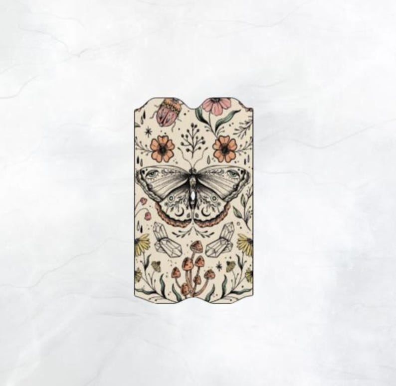 Puede incluir: Un marcap&aacute;ginas beige con una ilustraci&oacute;n de mariposa en blanco y negro rodeada de flores, setas y otros elementos bot&aacute;nicos.