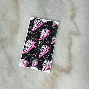 May include: A black and white sticker with a pink lightning bolt pattern. The sticker has a glittery finish.