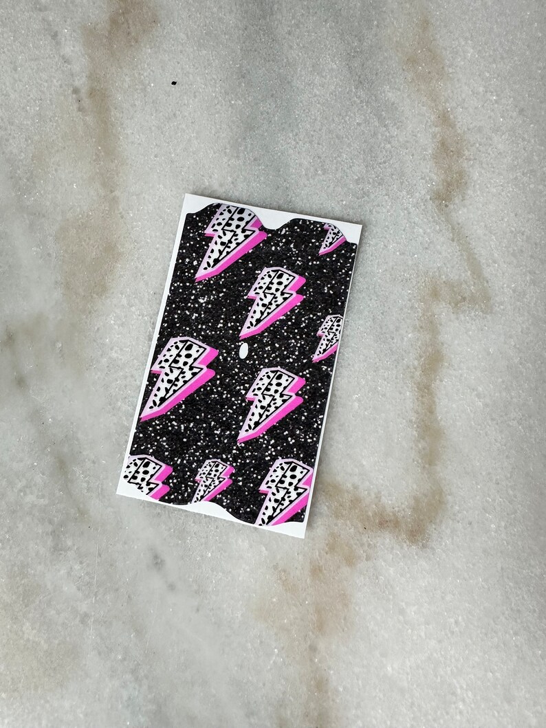 May include: A black and white sticker with a pink lightning bolt pattern. The sticker has a glittery finish.
