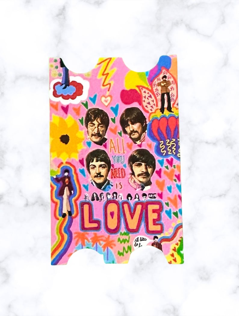 May include: A pink and colorful sticker with a psychedelic design featuring the Beatles. The sticker has the text "All you need is love" and images of the band members.