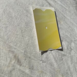 May include: A gold-colored, rectangular sticker with a wavy edge and a small hole in the center.