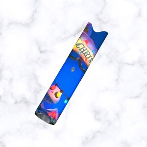 Puede incluir: Un bol&iacute;grafo vape azul y blanco con un dise&ntilde;o navide&ntilde;o que presenta un personaje con la nariz roja y una cadena de luces de colores. El texto "Chris" est&aacute; escrito en el lateral del bol&iacute;grafo.
