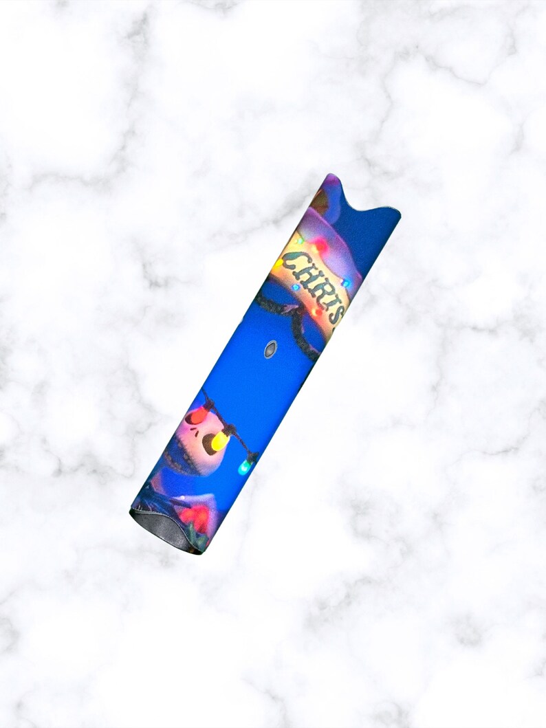 Puede incluir: Un bol&iacute;grafo vape azul y blanco con un dise&ntilde;o navide&ntilde;o que presenta un personaje con la nariz roja y una cadena de luces de colores. El texto "Chris" est&aacute; escrito en el lateral del bol&iacute;grafo.