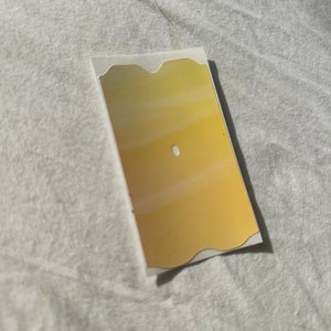 May include: A gold-colored sticker with a wavy edge and a white circle in the center. The sticker is on a white surface.