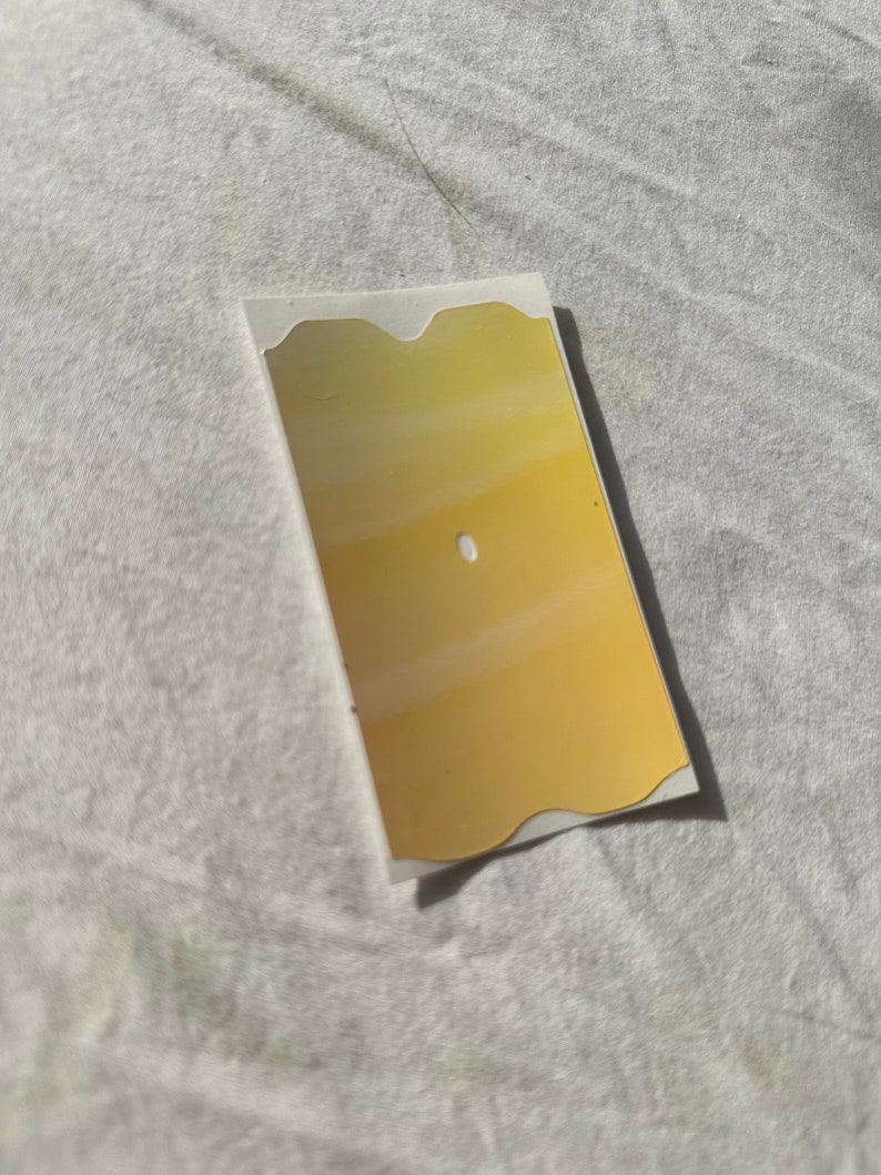 May include: A gold-colored sticker with a wavy edge and a white circle in the center. The sticker is on a white surface.