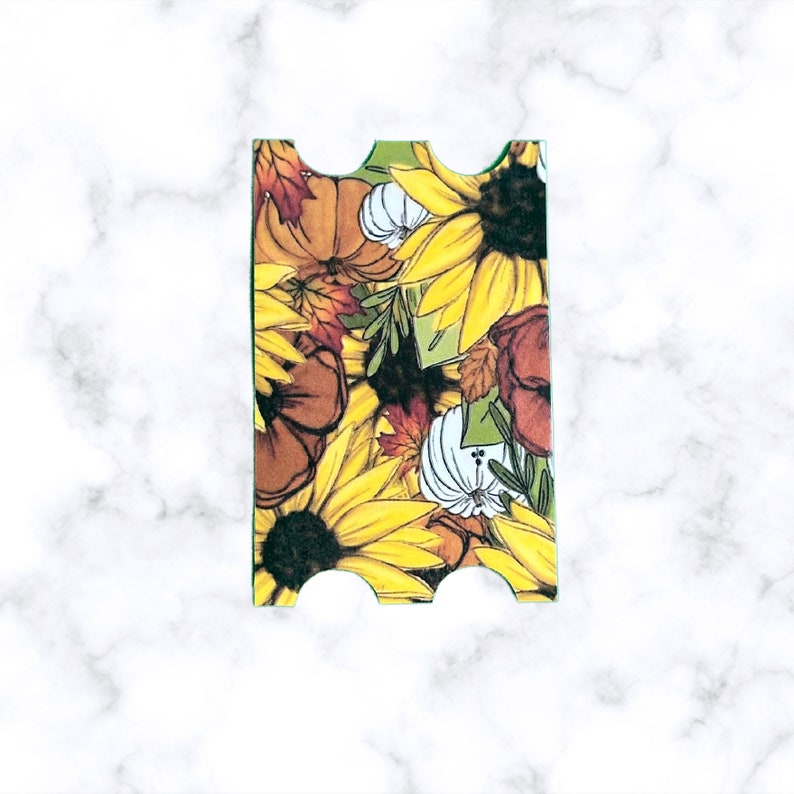 Pu&ograve; includere: Un segnalibro verde con un motivo floreale autunnale con girasoli, zucche e foglie. Il segnalibro ha un bordo smerlato.