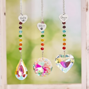 May include: Three rainbow crystal suncatchers with personalized heart-shaped tags. The tags read "Bailey", "Harley", and "Gracie". Each suncatcher features a different crystal shape: teardrop, round, and heart.