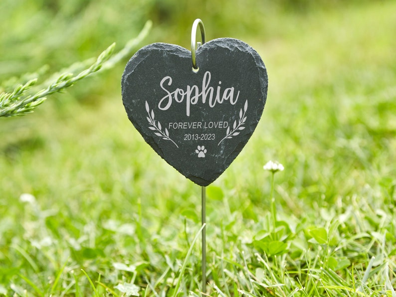 May include: Black heart-shaped slate garden marker with the name "Sophia" engraved, along with the text "Forever Loved 2013-2023" and a paw print.