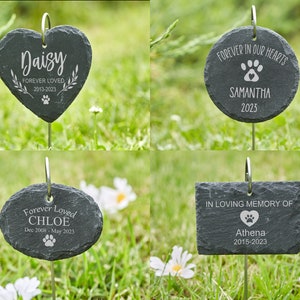 May include: Four different slate pet memorial markers with engraved text and paw prints. The markers are attached to metal stakes for placement in the ground. The markers are in the shape of a heart, circle, oval, and rectangle.