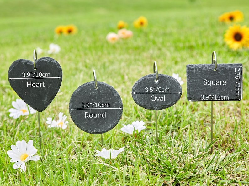 May include: Four black slate plant markers with different shapes: heart, round, oval, and square. Each marker has a metal stake and includes measurements in inches and centimeters.