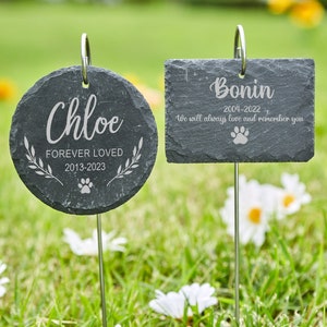 May include: Two black slate pet memorial markers with engraved text. The first marker is round and says "Chloe Forever Loved 2013-2023" with a paw print. The second marker is rectangular and says "Bonin 2004-2022 We will always love and remember you" with a paw print.