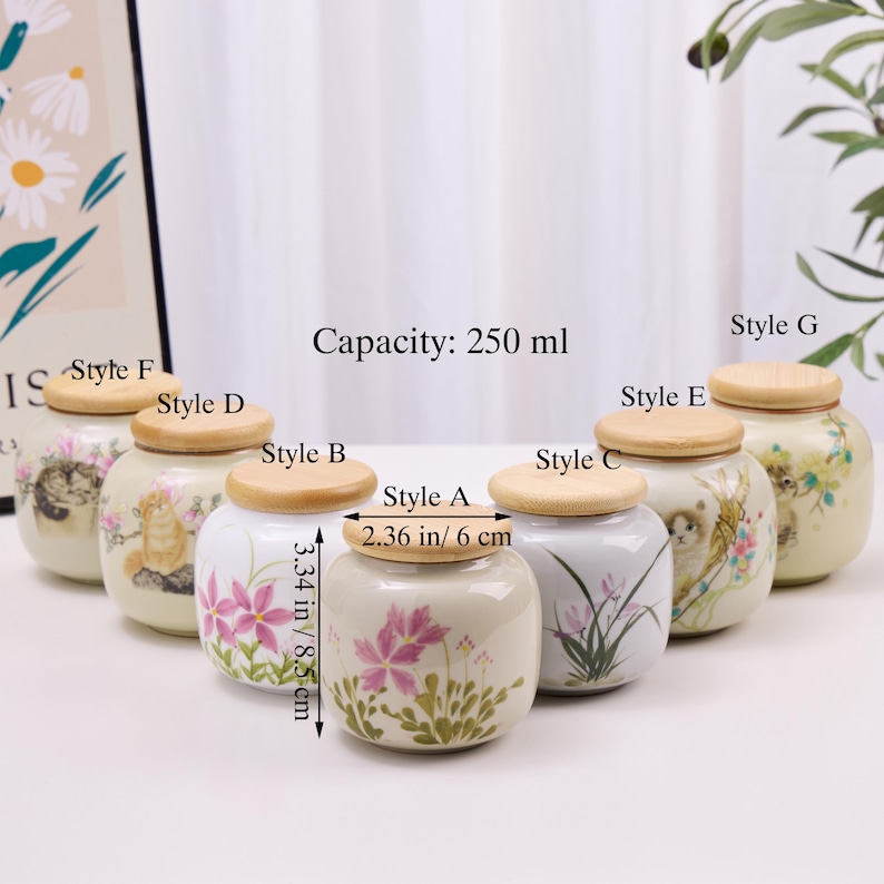 May include: A collection of ceramic jars with wooden lids, each adorned with floral or cat-themed designs. The jars are approximately 3.34 inches (8.5 cm) tall and 2.36 inches (6 cm) in diameter, with a capacity of 250 ml.