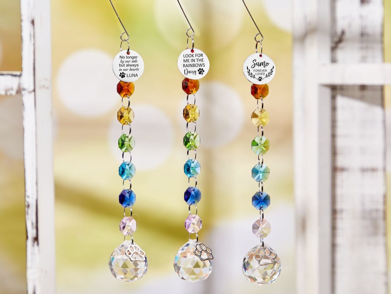 May include: Three rainbow crystal suncatchers with paw print charms and personalized memorial tags. The tags read "No longer by our side but always in our hearts LUNA", "Look for me in the rainbows Daisy", and "Sumo Forever Loved".