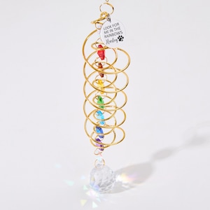 May include: A gold metal spiral with rainbow colored crystals hanging from it. A crystal ball hangs from the bottom of the spiral. A silver tag with the text "Look for me in the rainbows Harley" is attached to the top of the spiral.