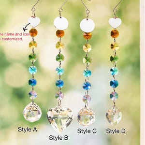 May include: Four hanging crystal suncatchers featuring vertical strands of multi-colored faceted beads in amber, yellow, green, blue, and clear. Each strand ends in a clear crystal shape with a paw print icon. Text reads: Only the name and icon can be customized.