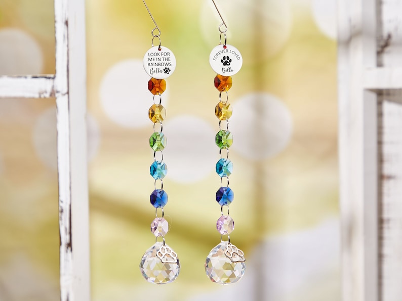 May include: Two rainbow crystal suncatchers with a silver charm at the bottom. The top charm on the left says "Look for me in the rainbows Bella" and the top charm on the right says "Forever Loved Bella".