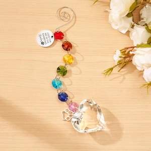 May include: A hanging ornament featuring a silver spiral hook, a round metal tag engraved with "LOOK FOR ME IN THE RAINBOWS" and a paw print, a vertical strand of multi-colored faceted crystal beads, a silver paw print charm, and a clear crystal heart.