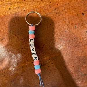 May include: A keychain with pink and blue beads spelling out the word "LOVER".