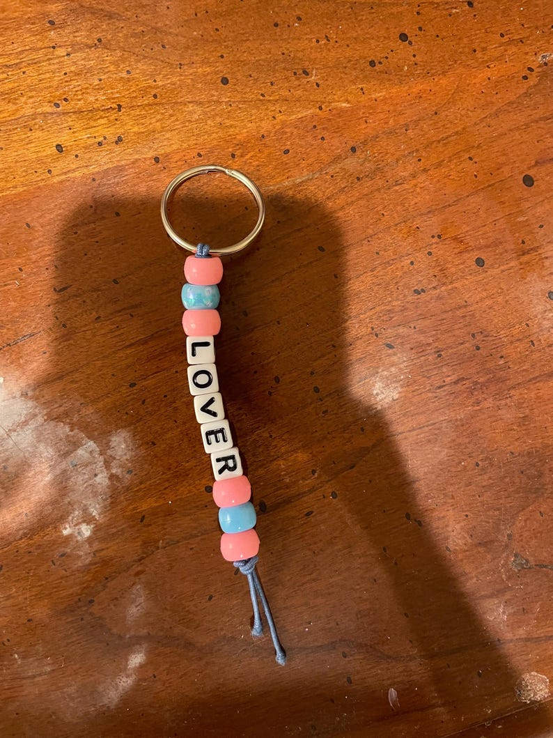 May include: A keychain with pink and blue beads spelling out the word "LOVER".