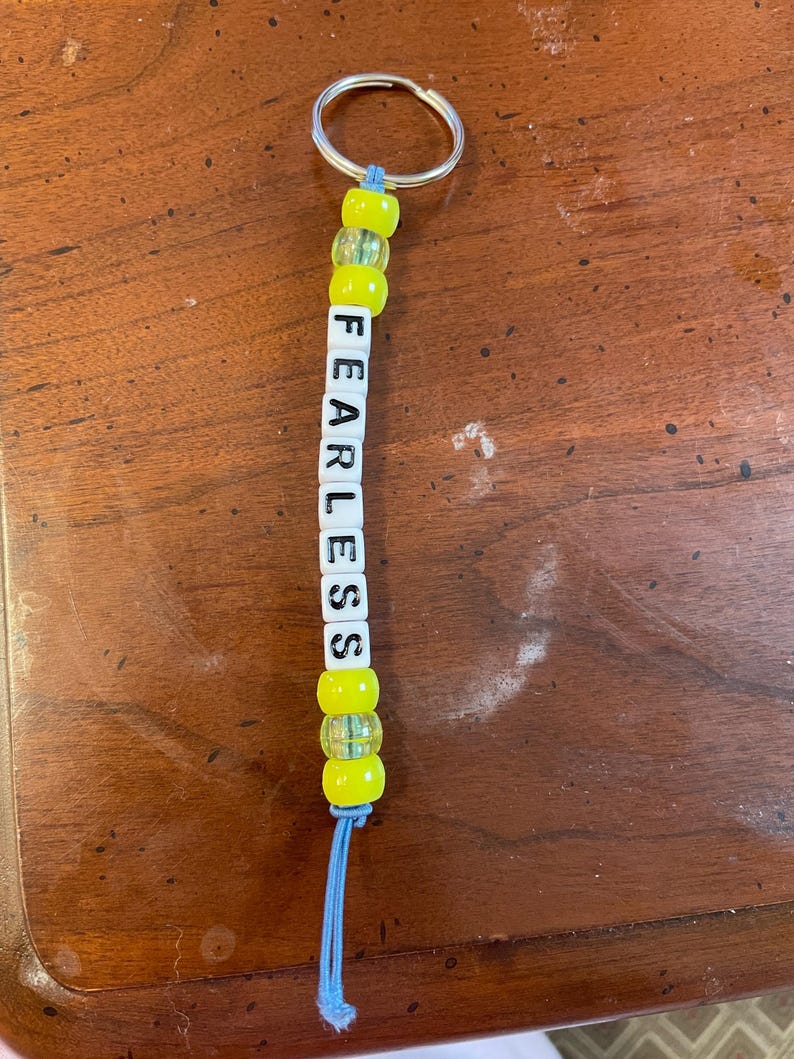 May include: A yellow and blue beaded keychain with the word "FEARLESS" spelled out in white letter beads.