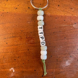 May include: A green and white beaded keychain with the letters "TIPPD" spelled out on the beads.