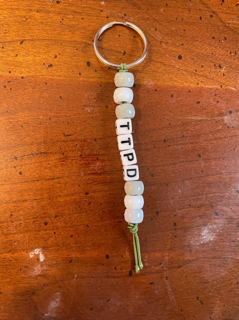 May include: A green and white beaded keychain with the letters "TIPPD" spelled out on the beads.