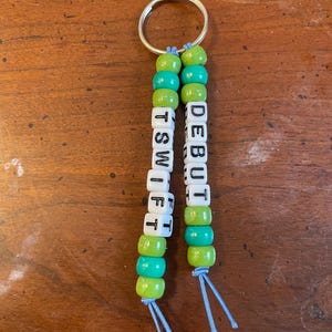 May include: A green and turquoise beaded keychain with the names "DEBUT" and "TSWIFT" spelled out in white letter beads.