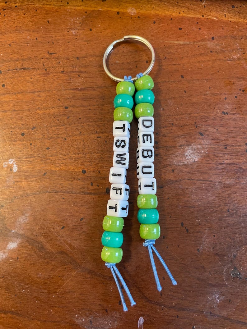 May include: A green and turquoise beaded keychain with the names "DEBUT" and "TSWIFT" spelled out in white letter beads.