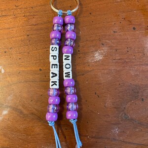 May include: Purple beaded keychain with the words "SPEAK NOW" on it.