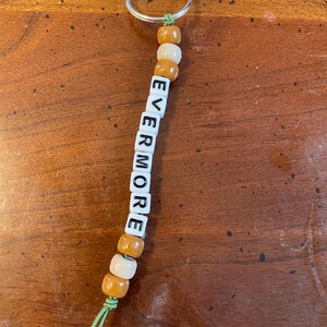 May include: A white and brown beaded keychain with the word "EVERMORE" spelled out in black letters.