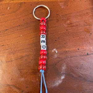 May include: Red beaded keychain with a silver key ring and a blue string. The beads spell out the word "RED".