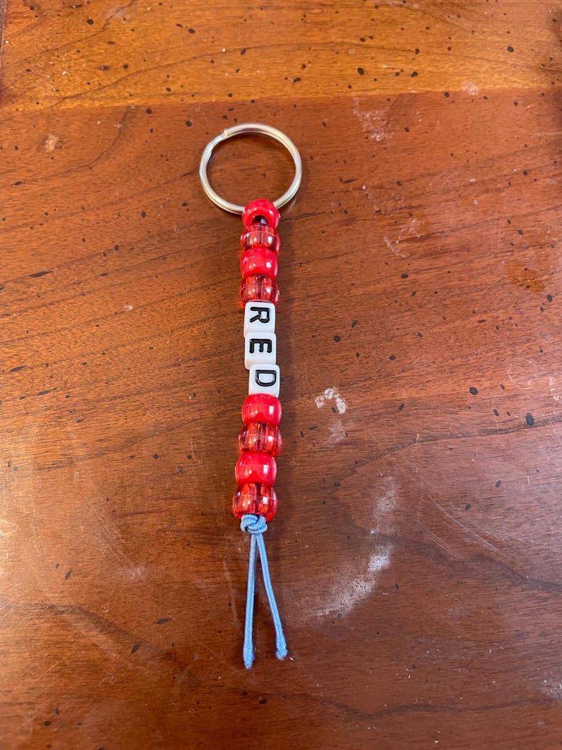 May include: Red beaded keychain with a silver key ring and a blue string. The beads spell out the word "RED".