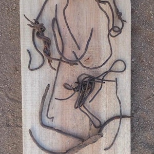 Può includere: Un'opera d'arte rustica con una tavola di legno marrone chiaro e un design astratto di fili metallici contorti marrone scuro. I fili arrugginiti sono disposti sulla superficie della tavola, creando un design astratto. L'opera ha un'estetica rustica.