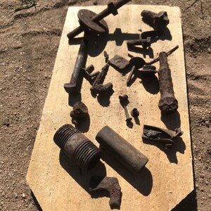 May include: A selection of rusty metal hardware, including bolts, nuts, and a threaded pipe, displayed on a light-coloured wooden board. The items are various sizes and shapes, showing signs of age and weathering.