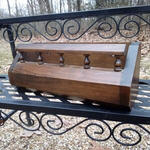 May include: A wooden shelf unit with five decorative finials. The shelf is stained a dark brown color and has a slightly distressed finish. The shelf is angled and appears to be made of solid wood.
