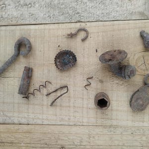 Könnte beinhalten: Eine Sammlung verschiedener rostiger Metallbeschläge, darunter eine große Ringschraube, ein Kronkorken, ein kleiner Haken, ein Gewinderohrstück, eine Sechskantmutter, eine kleine Riemenscheibe und mehrere verbogene Drahtfragmente mit brauner Patina.