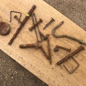 Peut inclure: Divers éléments de fixation métalliques rouillés, dont des vis, des clous et une agrafe, disposés sur une planche de bois brun clair. Les articles sont de tailles et de formes différentes, montrant des signes d'âge et d'usure.