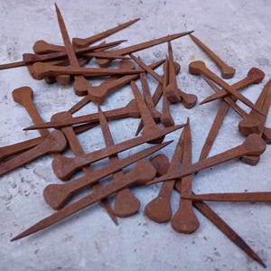 May include: A collection of rusty, antique nails, each with a hand-forged look. They have pointed ends and rounded, flattened heads. The nails are a warm, reddish-brown colour, indicating age and use. These are likely vintage or reclaimed.