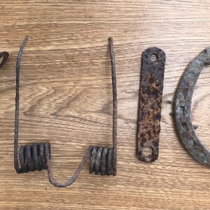 Peut inclure: Un ensemble de quatre objets métalliques usés comprenant un support incurvé, un mécanisme à double ressort, une barre plate rectangulaire avec deux trous circulaires et un fer à cheval usé, tous avec une finition rouillée, brune et grise.