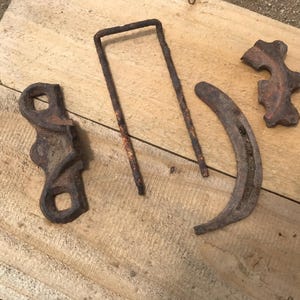 May include: Four weathered, rusty metal objects arranged on a wooden surface. The objects include a U-shaped piece, a curved piece, and two other irregularly shaped pieces. The metal has a dark brown color with areas of rust.