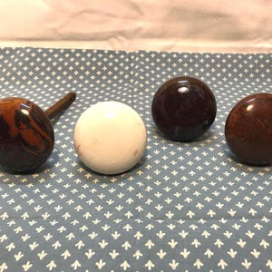 Op de afbeelding: Een verzameling houten knoppen en een trekker. De knoppen zijn in verschillende kleuren, waaronder een witte knop, een donkerbruine knop en een bruine knop met een houtnerfpatroon. De trekker is donkerbruin met een ronde knop.