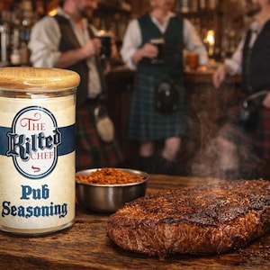 Könnte beinhalten: Ein Glas "The Kilted Chef Pub Seasoning" mit Holzdeckel steht neben einer kleinen Schüssel mit Gewürzen und einem gebratenen Steak auf einer Holzoberfläche. Das Glas hat ein blau-weißes Etikett. Dampf steigt vom Steak auf.